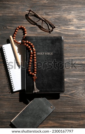 Holy Bible, notebooks, prayer beads, eyeglasses and pen on wooden background