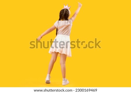 Little girl in crown with chalk piece on yellow background, back view. Children's Day celebration Royalty-Free Stock Photo #2300169469