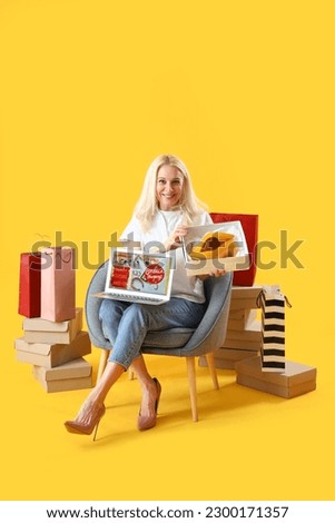 Mature woman with laptop and new shoes shopping online on yellow background