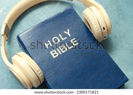 Holy Bible with headphones on blue background