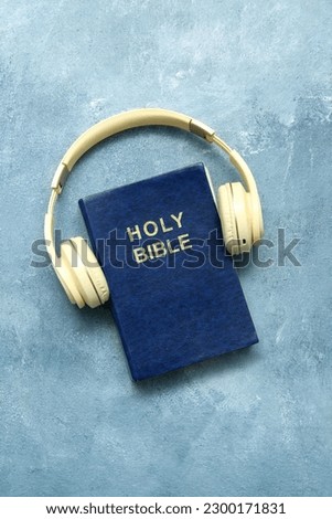 Holy Bible with headphones on blue background