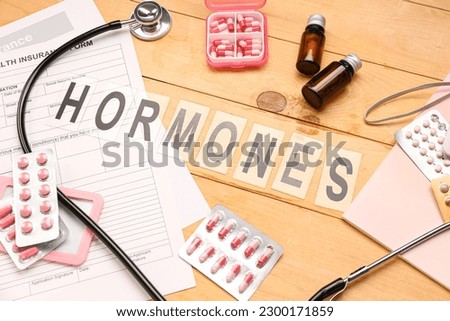Word HORMONES with pills and medical supplies on wooden background Royalty-Free Stock Photo #2300171859