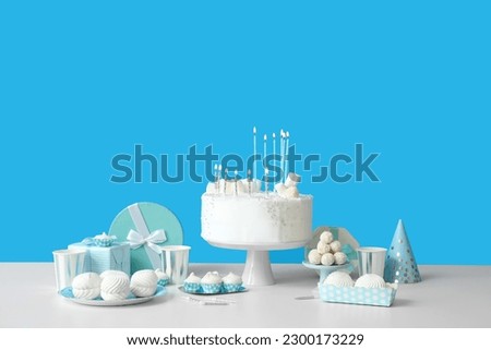 Birthday cake with candles and sweets on white table near blue wall