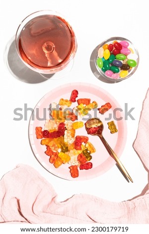 Plate with gummy bears, jelly beans and a glass with a pink drink. Coloring in food. Parties and celebrations