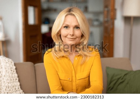 Portrait Of European Senior Lady Posing Expressing Positive Emotions, Smiling To Camera Sitting On Sofa In Living Room At Home. Shot Of Confident Blonde Mature Woman. Ageless Elegance And Beauty Royalty-Free Stock Photo #2300182313
