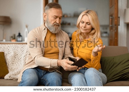 Financial Struggle. Unhappy Senior European Couple Looking At Empty Wallet With No Money, Suffering From Economic Crisis Sitting On Sofa At Home. Distressed Spouses Facing Finance Hardship Together Royalty-Free Stock Photo #2300182437