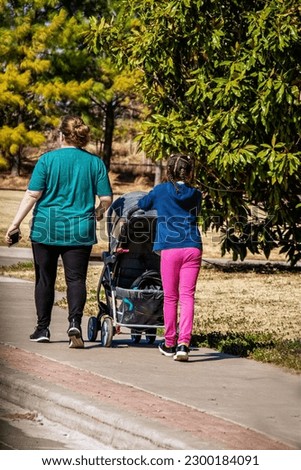 White mother with black daughter pushing baby carriage walking on trail with trees surrounding-selective focus
