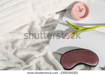 Sleep mask, tulip flower and alarm clock on fluffy blanket