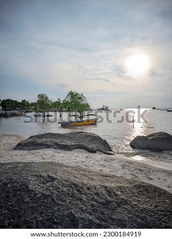 Putat Beach - Bangka Belitung Island: lots of rocks on the beach and calm water currents, fishing boats can be seen from a distance