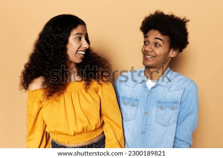 Young good-looking boyfriend and girlfriend flirting with each other against brown background, girl laughing at joke looking in his eyes, guy fooling around, showing his affection and interest