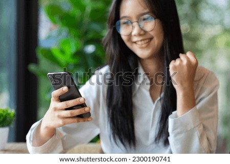 Happy Young Asian woman holding smartphone and arms raised gladly with winning prize.