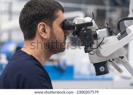 Focused doctor looking in innovative dental microscope to see teeth of patient in details professional medical equipment for cavity checkup bearded dentist in modern clinic Royalty-Free Stock Photo #2300207579