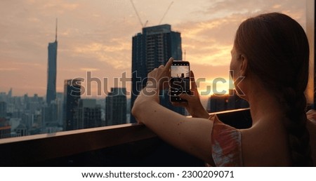Tourist woman taking photo of cityscape skyscrapers at sunset in capital of Malaysia. Cloudy twilight skyline view from the roof of an apartment building.