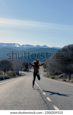 photo of woman seen from behind jumping in the middle of road