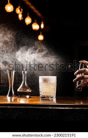 Penicillin classic cocktail in the glass. Bartender is spraying whiskey over Penicillin coctail. Alcohol cocktail with whiskey, lemon juice, and honey-ginger syrup named Penicillin Royalty-Free Stock Photo #2300215191