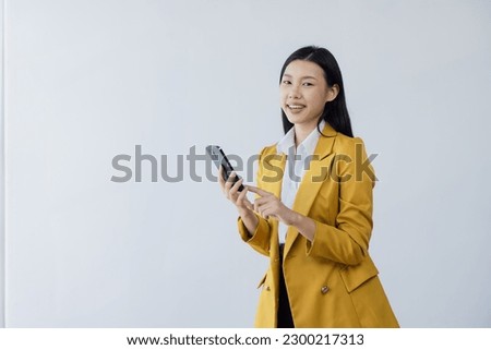 Happy young asian woman wearing a bright yellow suit and using smartphone standing on white background, Young asian woman. 
