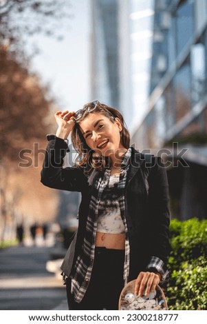 Modern, beautiful and young executive: sophisticated woman with sunglasses, backpack and skateboard in urban park in business district