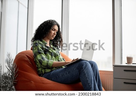 Attractive african american lady in casual apparel typing on portable computer while working remotely in office interior. Confident self-employed professional searching information for presentation.