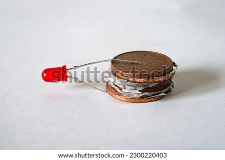 Battery consisting of a stack of copper coins with pieces of aluminum foil and filter paper dipped in vinegar. This will cause a small electric current to flow and the LED will light up. Voltaic pile. Royalty-Free Stock Photo #2300220403