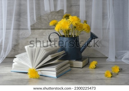 Still life of yellow dandelions and an open book with a dandelion in the form of a bookmark. Lightweight and graceful!