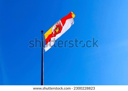 Flag and coat of arms of Grudziadz on a flagpole against a blue sky, Poland.