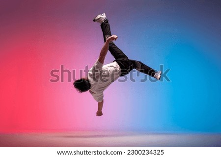 guy acrobat doing back fat in new lighting, male dancer jumps and falls in the air on red blue background, hiphop performer does trick and levitates in the air Royalty-Free Stock Photo #2300234325
