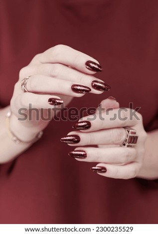 Woman hand with long nails and a bottle of dark red burgundy nail polish