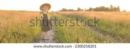 A little blonde girl in a straw hat walks in a field with a bouquet of daisies. The concept of walking in nature, freedom and an eco-friendly lifestyle.