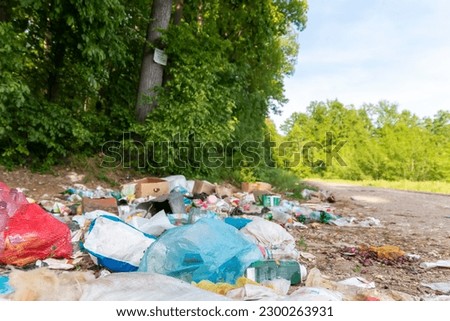 Piles of garbage in the forest, random dumping in nature. Stink heap, plastic bag and bottles, rubbish in polluted green  grass of nature landscape background. The concept of human pollution of forest Royalty-Free Stock Photo #2300263931