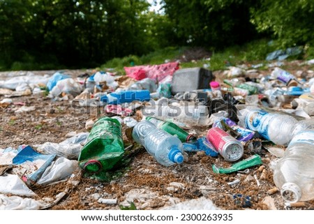 Piles of garbage in the forest, random dumping in nature. Stink heap, plastic bag and bottles, rubbish in polluted green  grass of nature landscape background. The concept of human pollution of forest Royalty-Free Stock Photo #2300263935