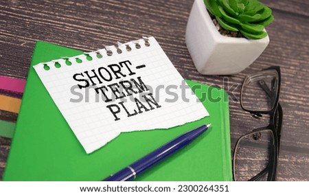 Notebook with text SHORT-TERM PLAN on a table with charts,pen and glasses Royalty-Free Stock Photo #2300264351