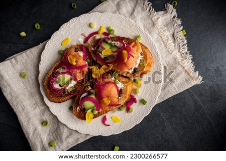 Smoked-salmon crostini with cream cheese and cucumber. Garnished with pickled red onions, scallions, and daffodil petals. Royalty-Free Stock Photo #2300266577