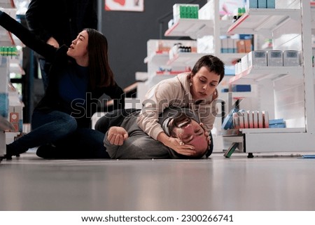 Drugstore client holding man head during epilepsy attack, providing first aid. Diverse women rescuing pharmacy store customer during epileptic disorder seizure in apothecary Royalty-Free Stock Photo #2300266741
