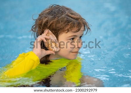 Kid listening to the ocean in a shell. Little boy holding a seashell close to his ear. Child play with shell at the beach. Little child in swimwear playing on tropical beach in summer day. Listening Royalty-Free Stock Photo #2300292979