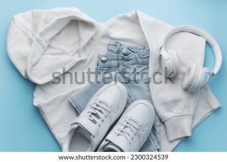 Childs clothing, accessories, footwear,  sweatshirt,  jeans,  sneakers, headphones on blue background. Outfit for teens. Top view, flat lay. Trendy colors
