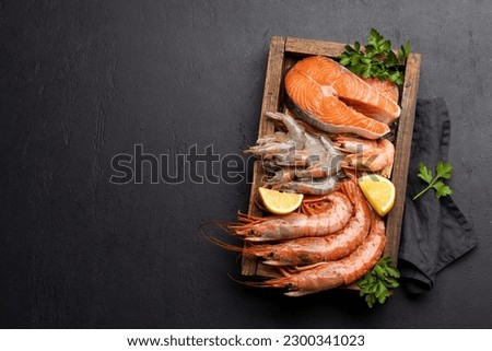 A top view of fresh seafood such as shrimp, langoustines, and trout steaks in wooden box. Flat lay with copy space Royalty-Free Stock Photo #2300341023