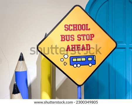 Close-up of a School Bus Stop Ahead Sign with pencil and door background. Warning road sign telling drivers that there is a bus stop ahead. Concept for back to school, holiday end, new academic year.