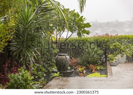 A photo of a subtropical small backyard garden during a heavy rainstorm. Raindrops are seen as vertical lines on the image.Warm tones.