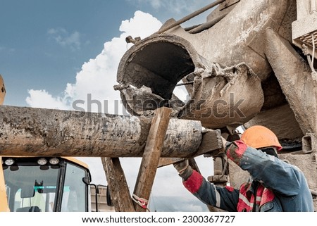Mixer truck is transport concrete to the casting place on building site. Concrete is flowing into the foundations of the building. The worker directs the concrete to the place of pouring Royalty-Free Stock Photo #2300367727