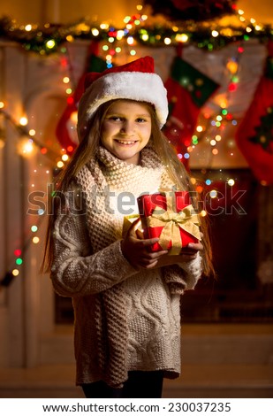 Beautiful little girl in red hat holding sparkling gift box 