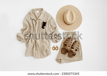 Aesthetic summer fashion composition with neutral beige female clothes and accessories. Muslin tee blouse, shorts, straw hat, leather sandals, sunglasses, earrings. Flat lay, top view.