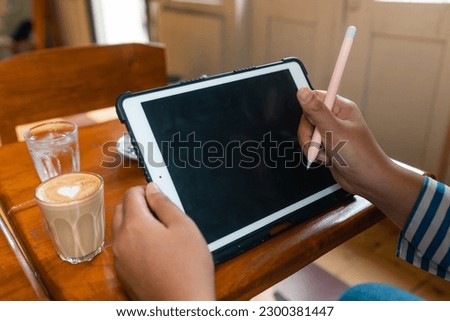 close up of asian woman drawing on a tablet using a tablet pen while she enjoying her coffee and breakfast on a wooden table. Hands On Technology concept