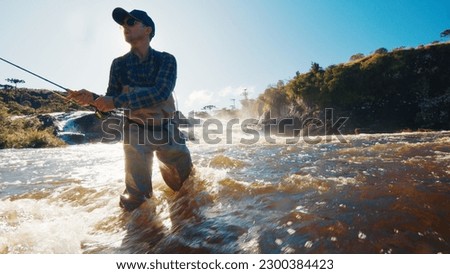 Fly fishing. Fisherman in waders casts the line on the rapid murky river Royalty-Free Stock Photo #2300384423