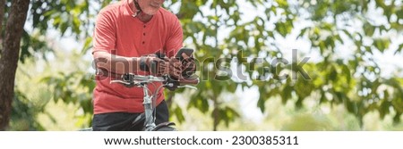 Close up Asian Senior man Hands using mobile phone or smartphone for online application while travel with bicycle outdoors. Searching GPS coordinates. Grandfather exercising with bike riding. Banner.