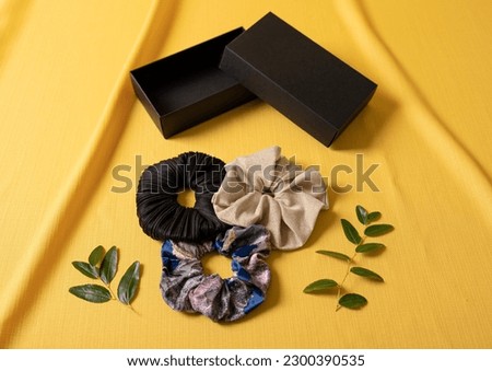 Three scrunchies and their box at yellow background. They are on sale.