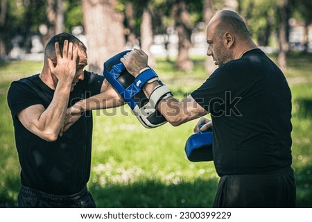 Muay thai trainer holds focus mitts. Elbow kick technique training and demonstration with pads. Martial arts practice Royalty-Free Stock Photo #2300399229