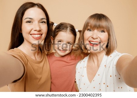 Close up happy women wear casual clothes with child kid girl 6-7 years old. Granny mother daughter do selfie shot pov on mobile cell phone isolated on plain beige background Family parent day concept