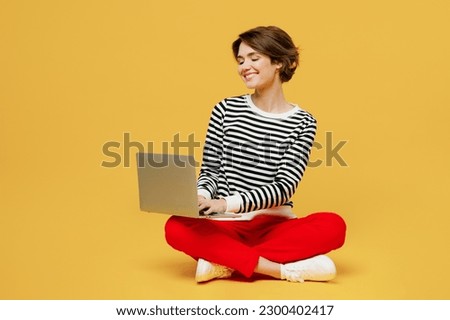 Full body smiling young IT woman wear casual black and white shirt sit hold use work on laptop pc computer surfing internet isolated on plain yellow color background studio portrait. Lifestyle concept
