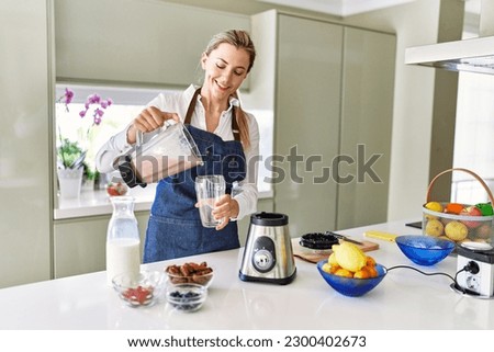 Young blonde woman smiling confident pouring smoothie on glass at kitchen