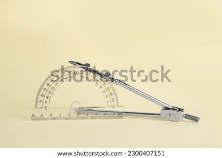 Protractor and metal compass on yellow background